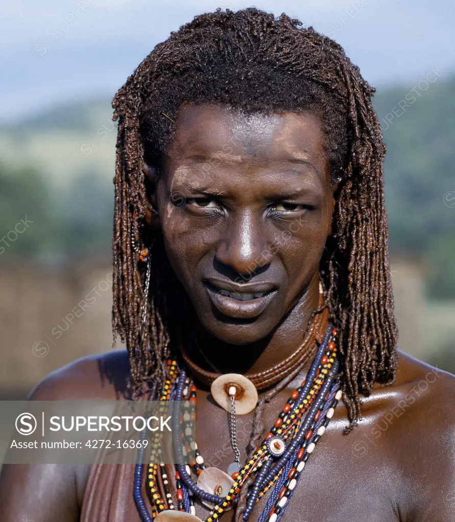 A Maasai warrior resplendent  with long ochred braids. His body has been smeared with red ochre mixed with animal fat while parts of his face have been covered with  ochre powder.