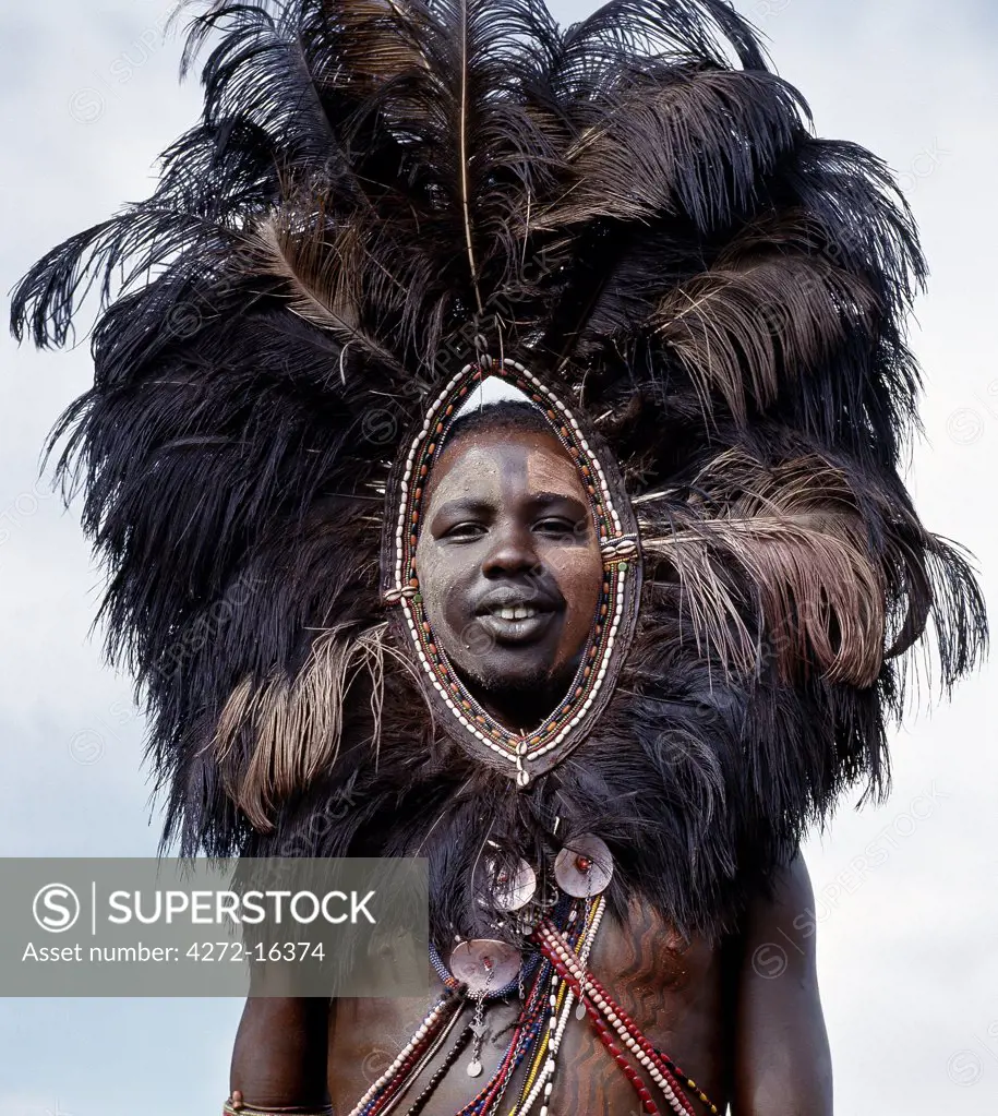 A Maasai warrior, his face and body decorated with red ochre and clay, wears an ostrich feather headdress. This singular adornment was once worn by warriors going into battle and was likely designed to frighten an enemy.