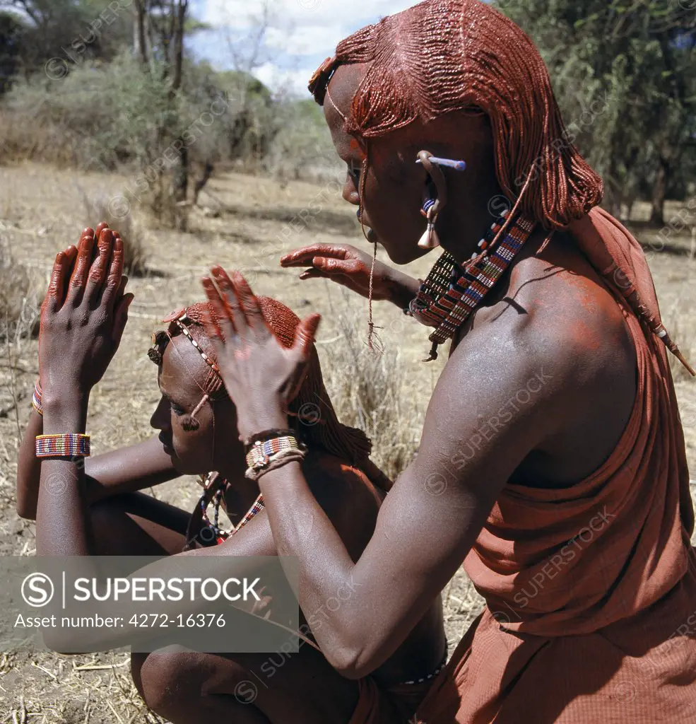 A Maasai warrior resplendent with long ochred braids tied in a pigtail at the back, puts red ochre on his friend's plaits. Red ochre is anatural earth ,which is mixed with animal fat to the consistency of greasepaint.