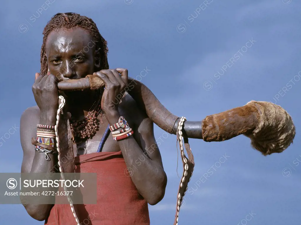 A Maasai warrior blows a trumpet fashioned from the horn of a Greater Kudu. The strap is decorated with cowrie shells.  Kudu-horn trumpets are only sounded to call men to arms or on ceremonial occasions.