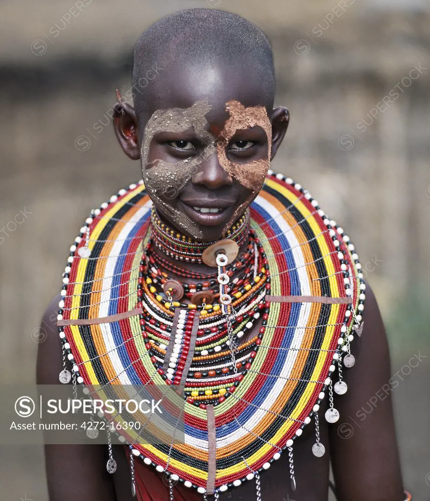 A young Maasai girl wears face paint and numerous beaded ornaments in preparation for a dance with warriors.