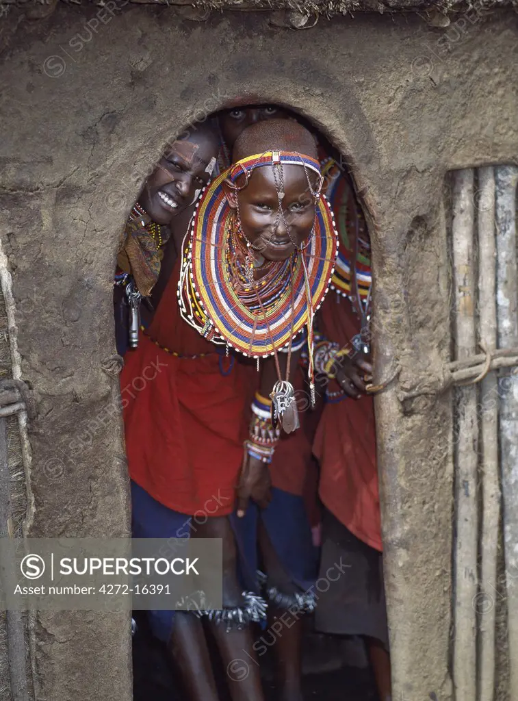 Maasai girls in all their finery and with bells tied round their legs wait at the entrance to a house before dancing with warriors.