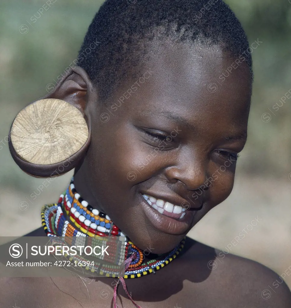 A young Maasai girl wearing a wooden plug in her pierced ear to elongate the earlobe. It has been a tradition of the Maasai for both men and women to pierce their ears and elongate their lobes for decorative purposes. Her two lower incisors have been removed - a common practice that may have resulted from an outbreak of lockjaw a long time ago.