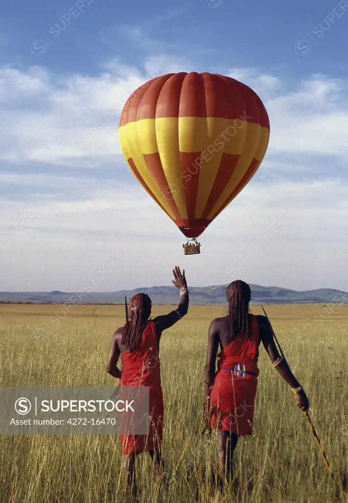 Two Maasai warriors watch a hot air balloon flight over Masai Mara.