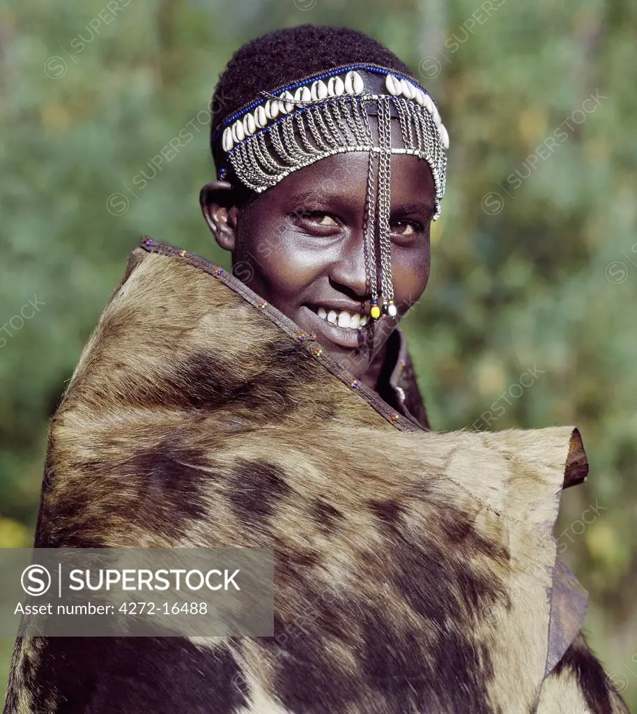A girl from the Ogiek community of hunter-gathers living in the Mau Forest keeps warm in a cowhide. Following Maasai custom, she wears a decorated headband which marks her recent circumcision.