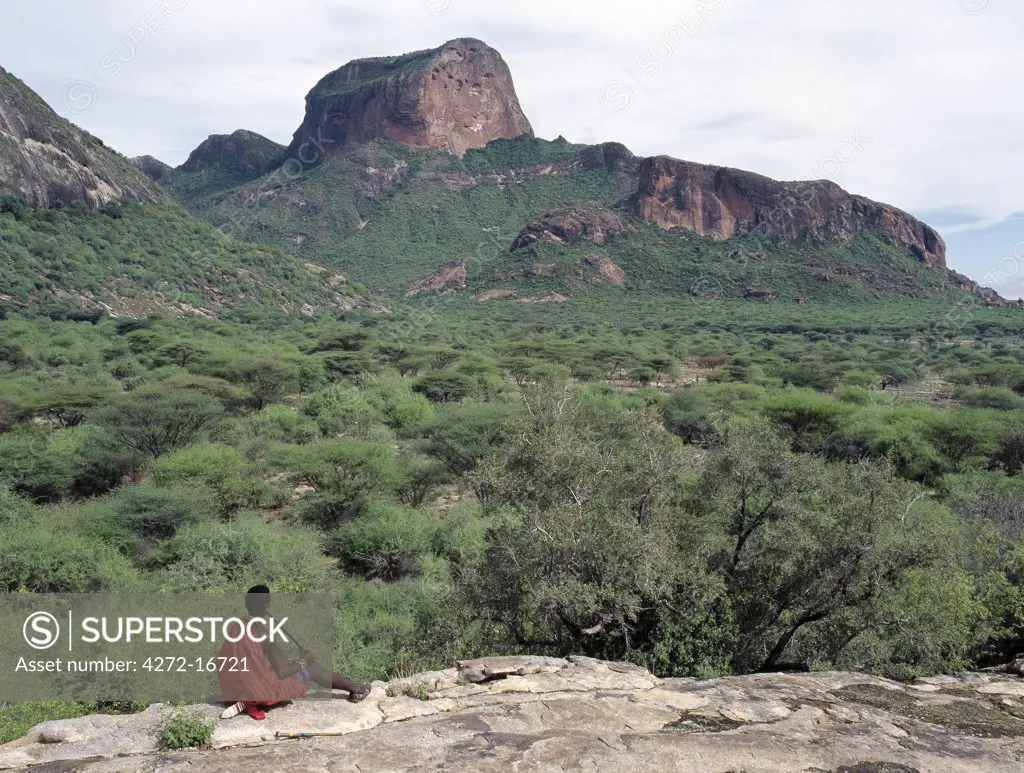 A Samburu warrior plays a homemade flute overlooking Poi, a prominent rock feature in the Ndoto Mountains of Samburuland. The Samburu of Northern Kenya are a semi-nomadic pastoral community related to their more famous cousins,  the _maa speaking Maasai.