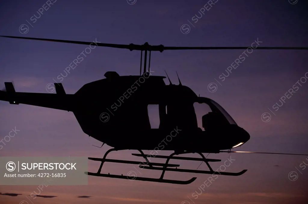 A Bell Long Ranger helicopter hovering at sunset