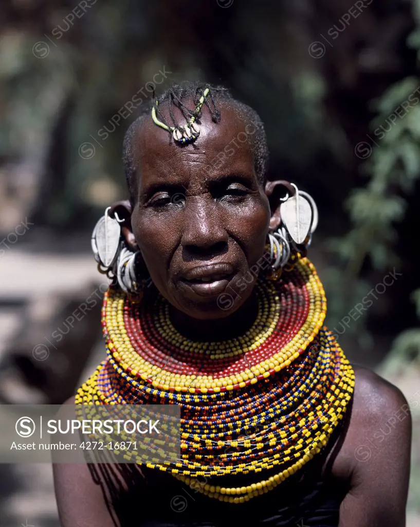 An old Turkana woman, typically wearing many layers of bead necklaces and a series of hooped earrings with an pair of leaf-shaped earrings at the front.