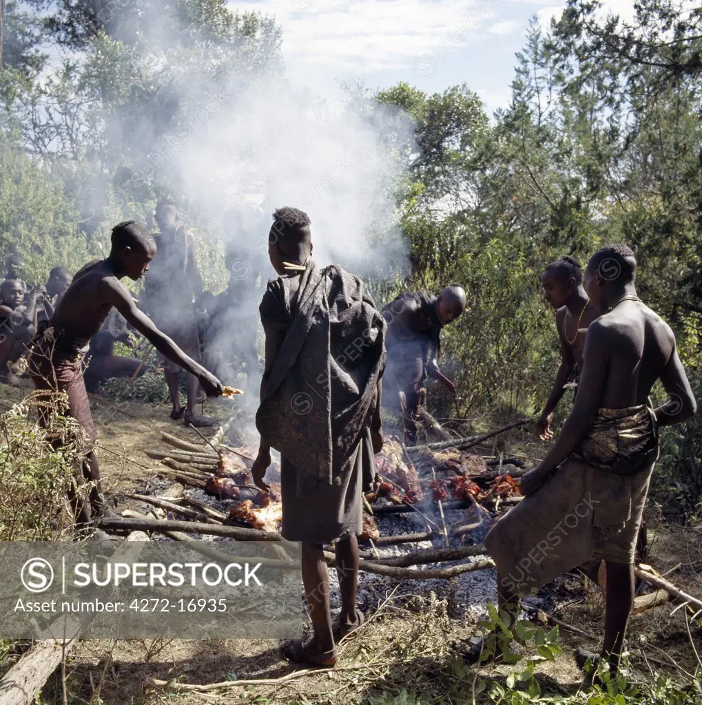 Samburu boys roast meat in the cedar forests of the Karisia Hills.   Several weeks before their initiation, boys must wear charcoal blackened cloaks, which are made by their mothers from three goatskins.