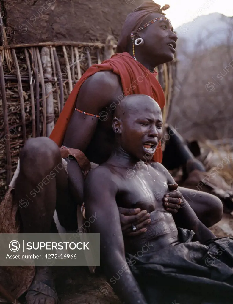 Early in the morning, a Samburu youth sings the lebarta, the Samburu circumcision song, just after he has been circumcised outside his mothers house. One of his sponsors attends him by holding his back. Boys are not allowed to show any sign of fear or pain.