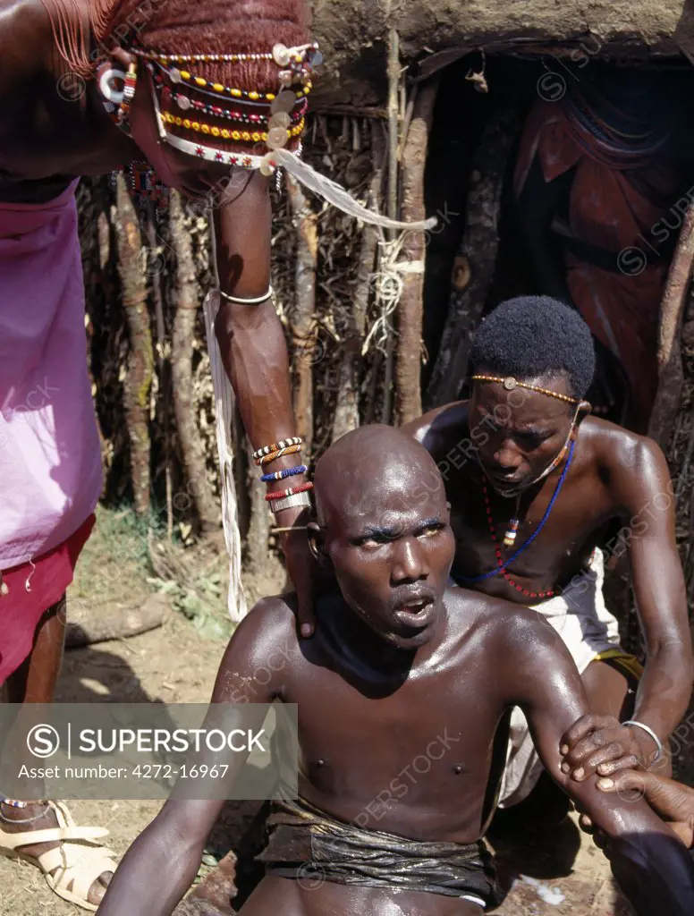 A Samburu youth sings the lebarta, the Samburu circumcision song, just after he has been circumcised outside his mother's house. His ritual sponsors attend him before lifting him into the house for a rest. Boys are not allowed to show any sign of fear or pain.