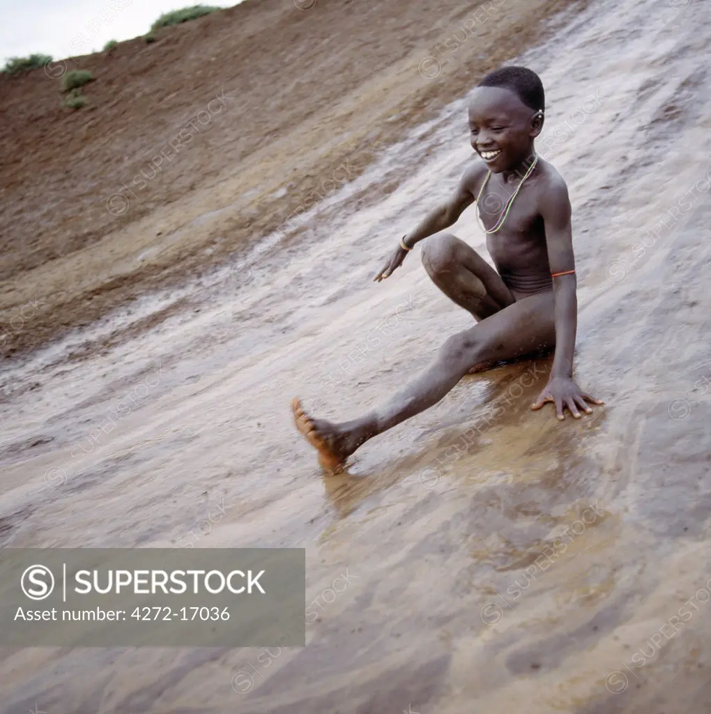 A young Samburu boy enjoys himself on a mudslide