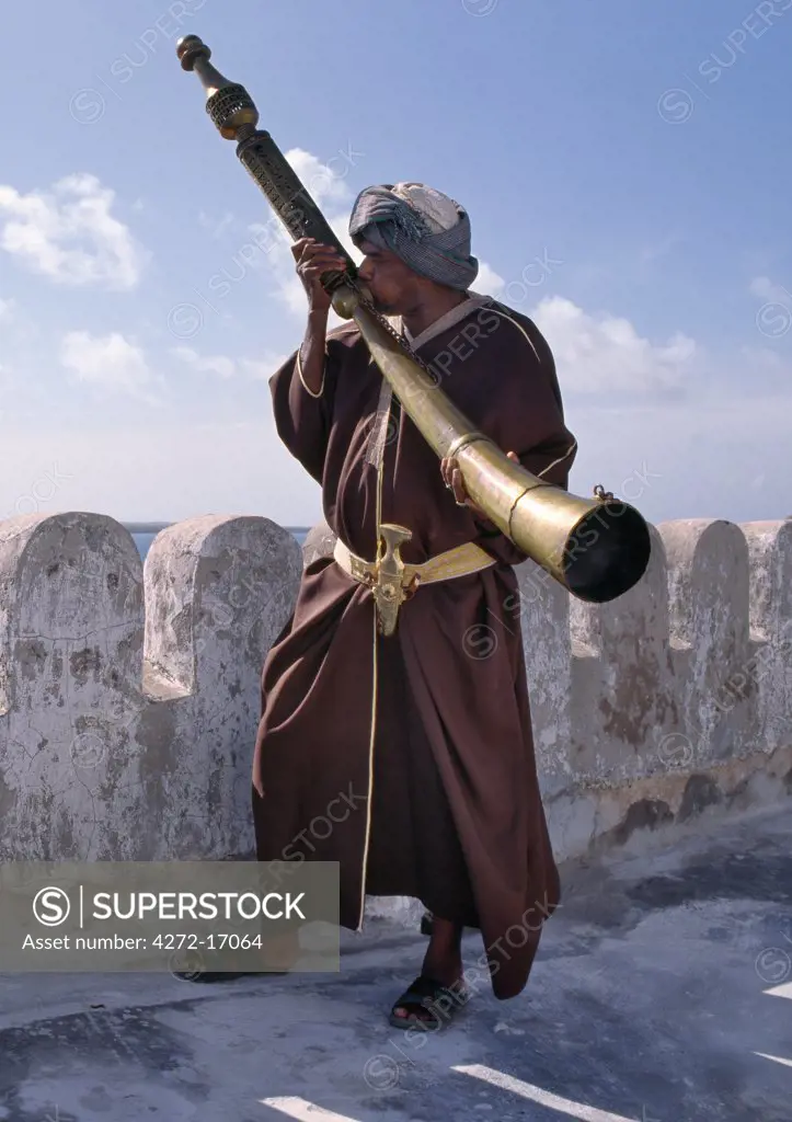 A Swahili man in traditional attire blows the Siwa on the battlements of the Lamu Museum. This unique and hugely heavy ritual horn was used before the 19th century in Pate and Lamu Islands to herald religious and festive occasions or to alert the community of danger.