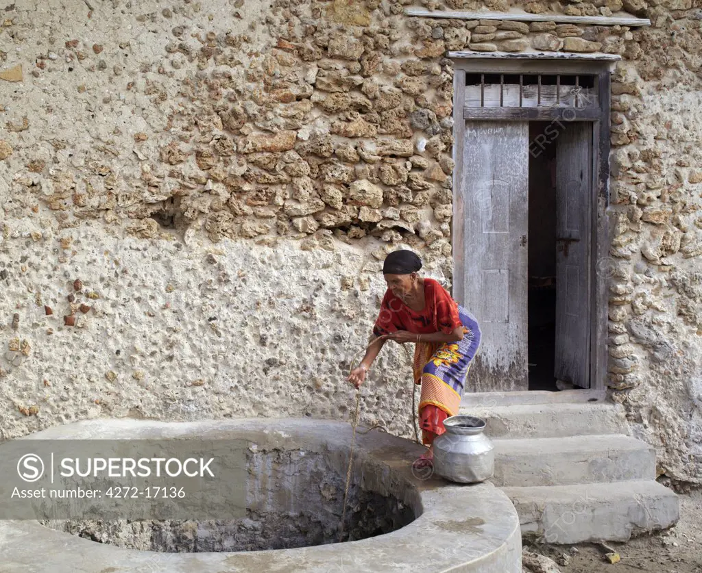 An old woman draws brackish water from a well outside her home in Faza village.  Her house, like most others in the village, is made of coral rag. The chequered history of Faza dates back several hundred years.