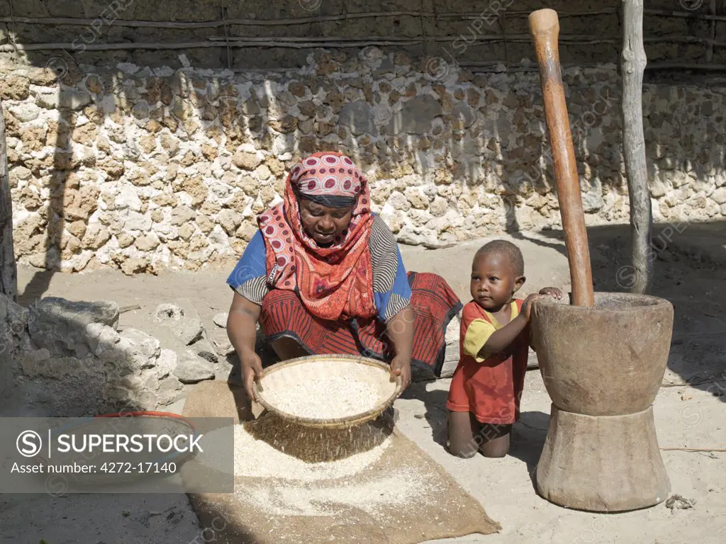 A Swahili woman winnows grain outside her home while her young son grasps a large pestle and mortar beside her. Her house, like most others in the village, is made of coral rag. The chequered history of Faza dates back several hundred years.