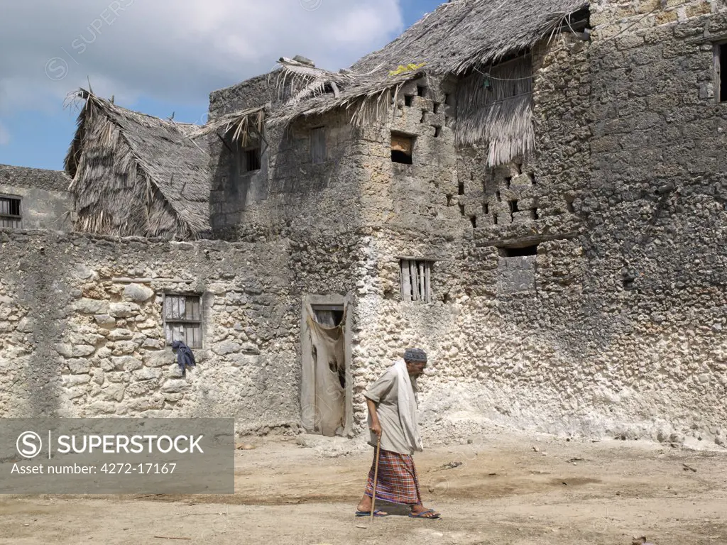 An elderly man strides past a large double storied building in Pate Village. All the buildings in Pate are constructed of coral rag with makuti roofs, which are a type of thatch made from coconut palm fronds. Pate was established by Arabs from Arabia in the 13th century, or possibly earlier.