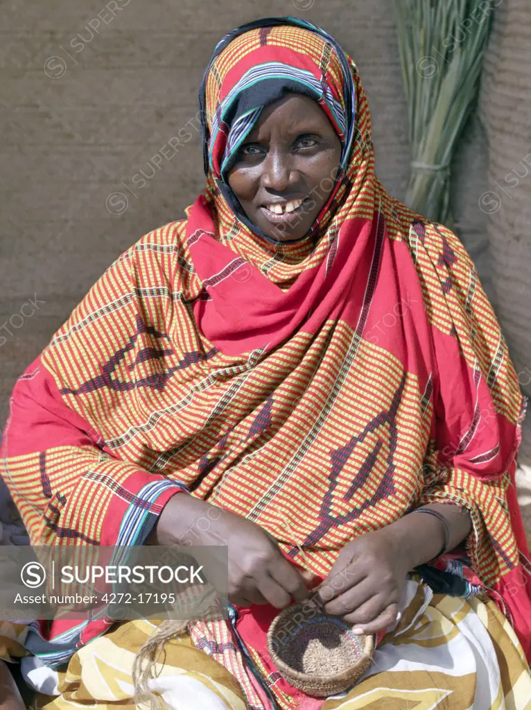 A Pokomo woman in bright cotton clothing makes a small woven basket. The Pokomo people are of Bantu origin and live along the banks of the Tana River southwest of Lamu.