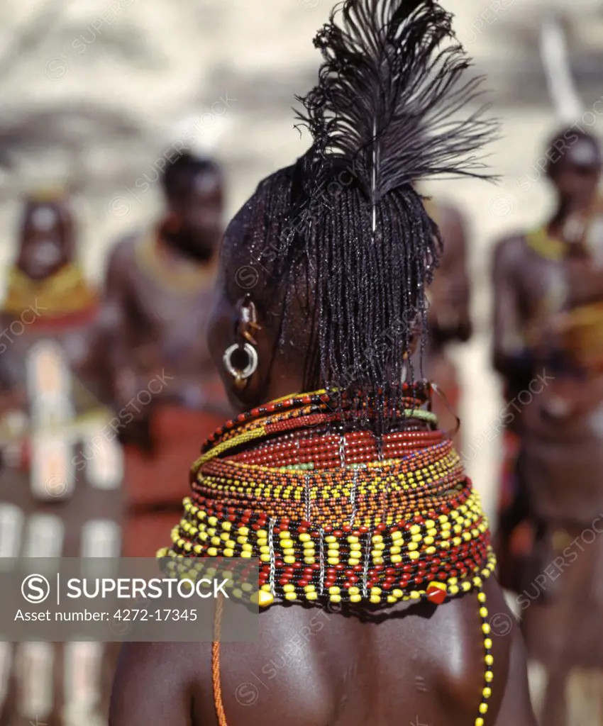 A Turkana woman with braided hair wearing heavy beaded necklaces and a black ostrich feather in the typical attire of Turkana married women.