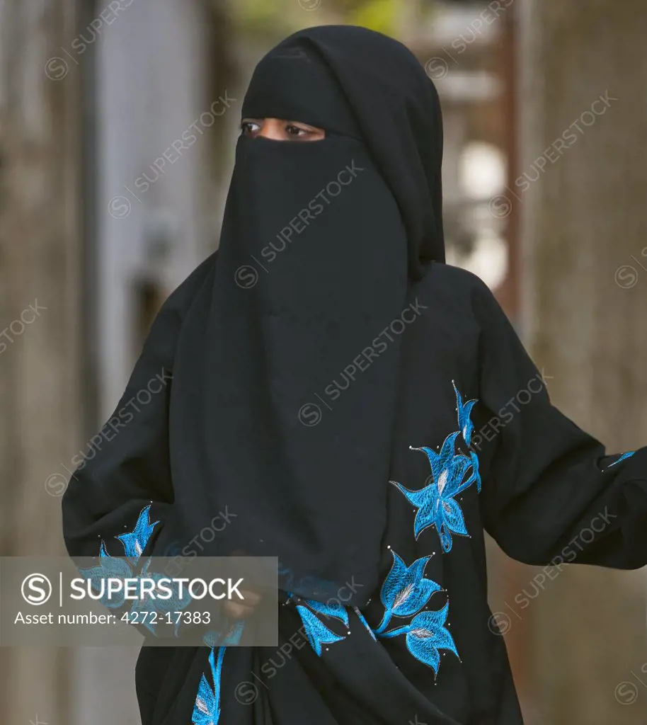 Kenya, Lamu Island, Lamu. A Muslim woman of Lamu town wearing a buibui or face veil but dressed in an attractive embroidered black dress.