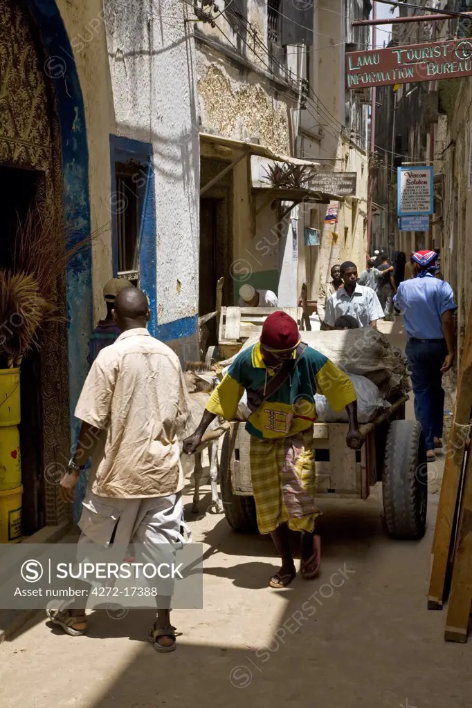 Kenya, Lamu Island, Lamu. A man pulls a hand cart along the narrow streets of Lamu town. Lamu is a World Heritage Site.