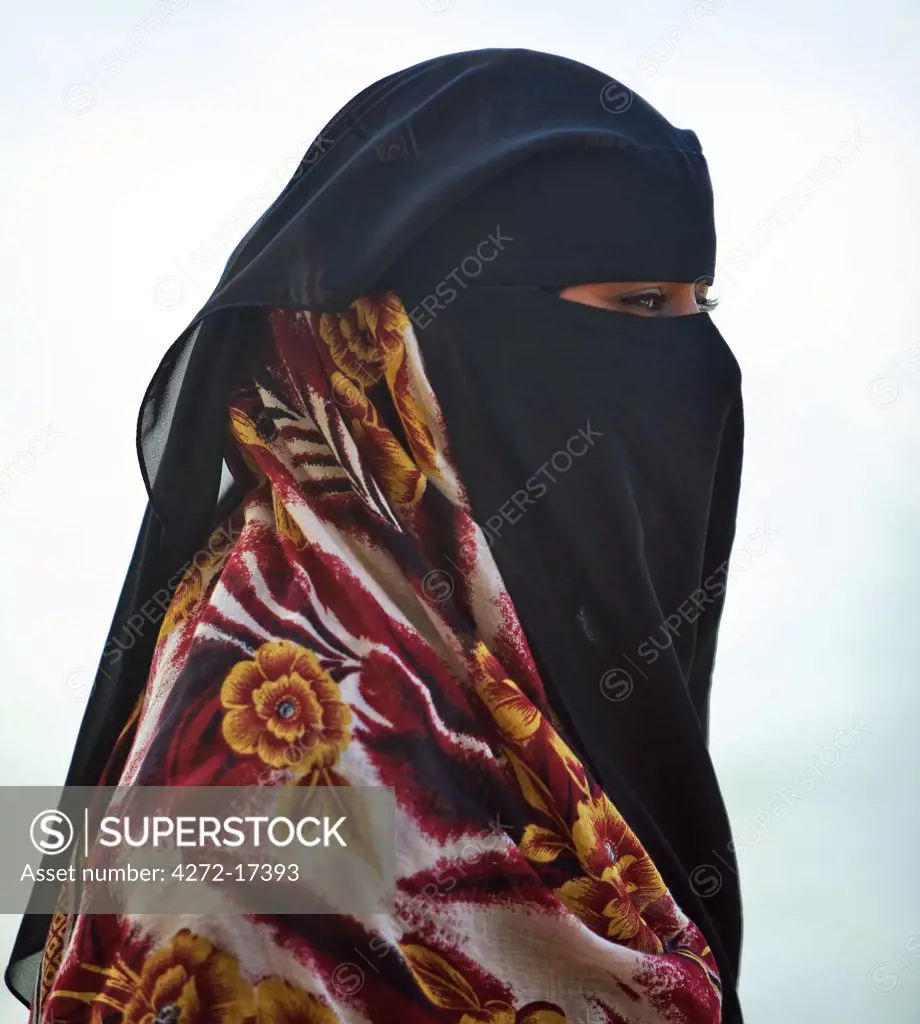 Kenya, Lamu Island, Shela. A Muslim woman with a face veil wearing a brightly coloured wrap.