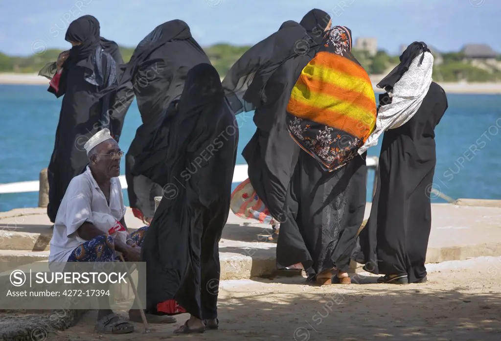 Kenya, Lamu Island, Shela. A group of Muslim women and an old man wait for a ferry boat at Shela pier.