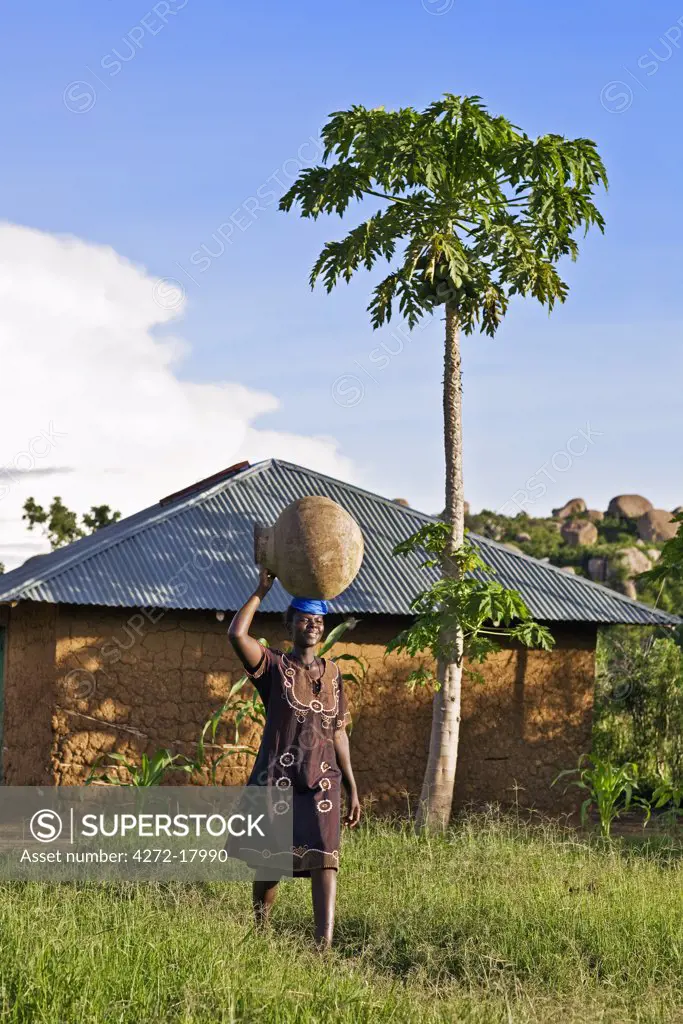 Kenya, Nyanza District. A Luo woman carries a large water pot to her home near Kit Mikayi, a culturally important site for the local Luo community.