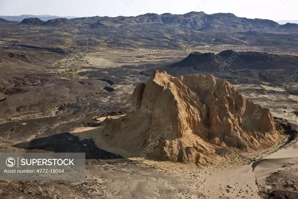 A crumbling extinct volcano, known as Aruba Rock, is surrounded by outflows of black lava rock on the edge of the Suguta Valley.
