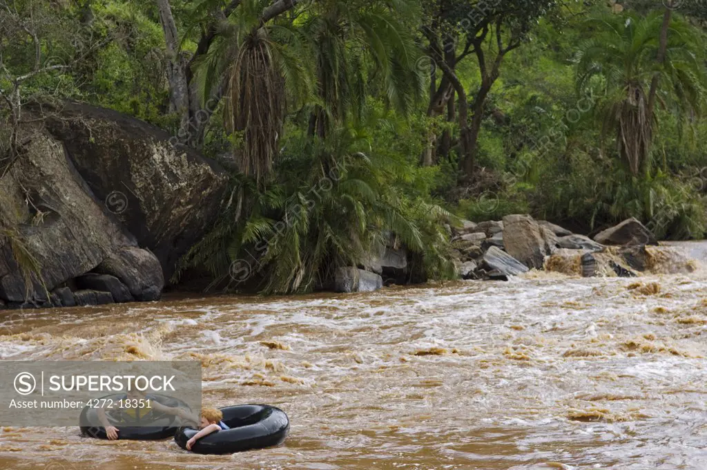 Kenya, Laikipia, Ol Malo.  Two boys ride down the rapids on the Ewaso Nyiro River in inner tubes. (MR)
