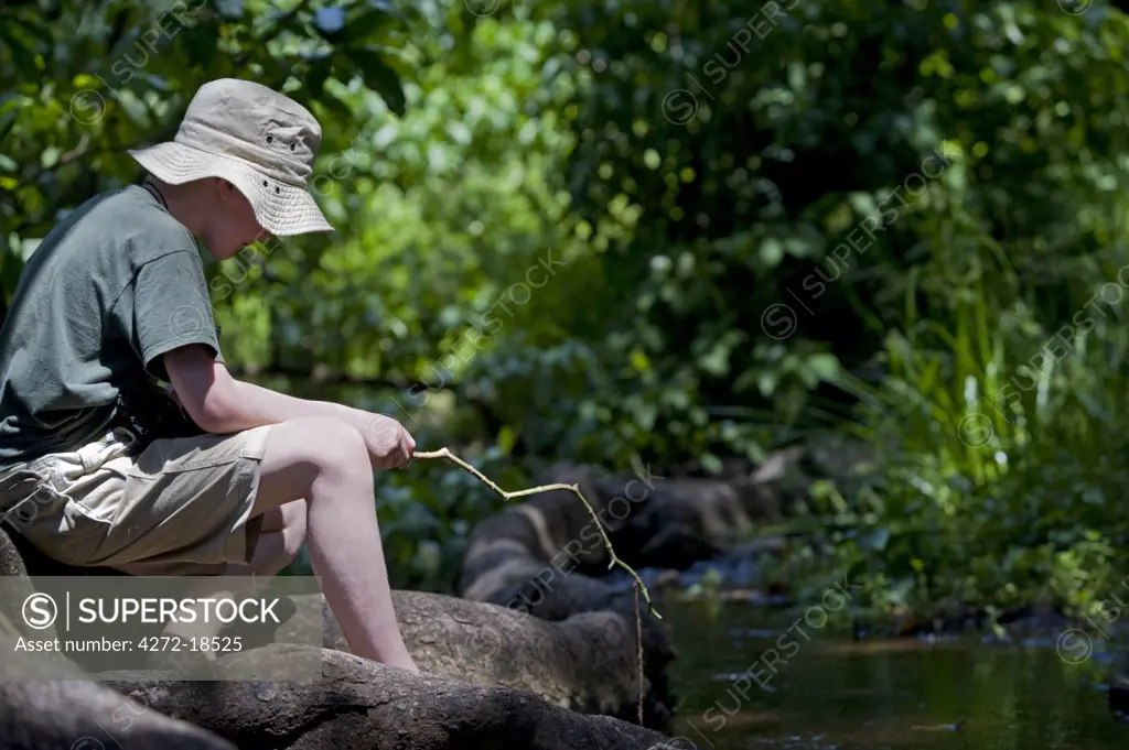Kenya, Laikipia, Lewa Downs.  A young boy on a family safari at Wilderness Trails, fishes in a stream.
