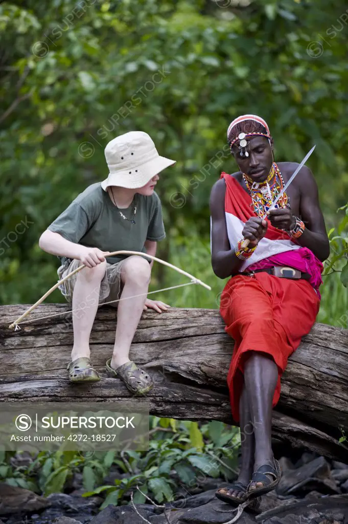 Kenya, Laikipia, Lewa Downs. One Wilderness Trails' Laikipiak Maasai guides shows child how to sharpen an arrow.