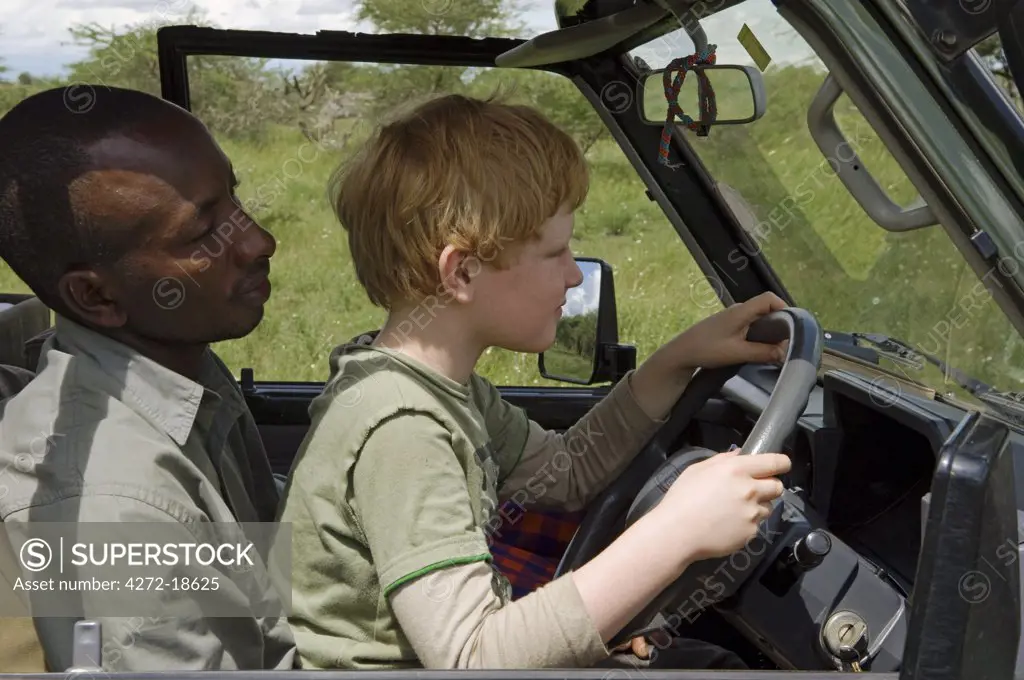 Kenya, Chyulu Hills, Ol Donyo Wuas. Safari guide, Moses Njoroge, lets a young guest drive the Landcruiser. (MR)