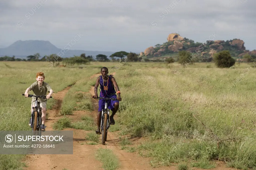 Kenya, Chyulu Hills, Ol Donyo Wuas.  A Maasai guide takes a child on a mountain biking safari.  (MR)