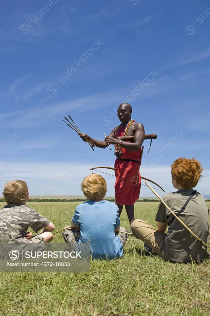 Kenya, Masai Mara. Safari guide, Salaash Ole Morompi, shows different tips on his Maasai arrows to boys on safari. (MR)