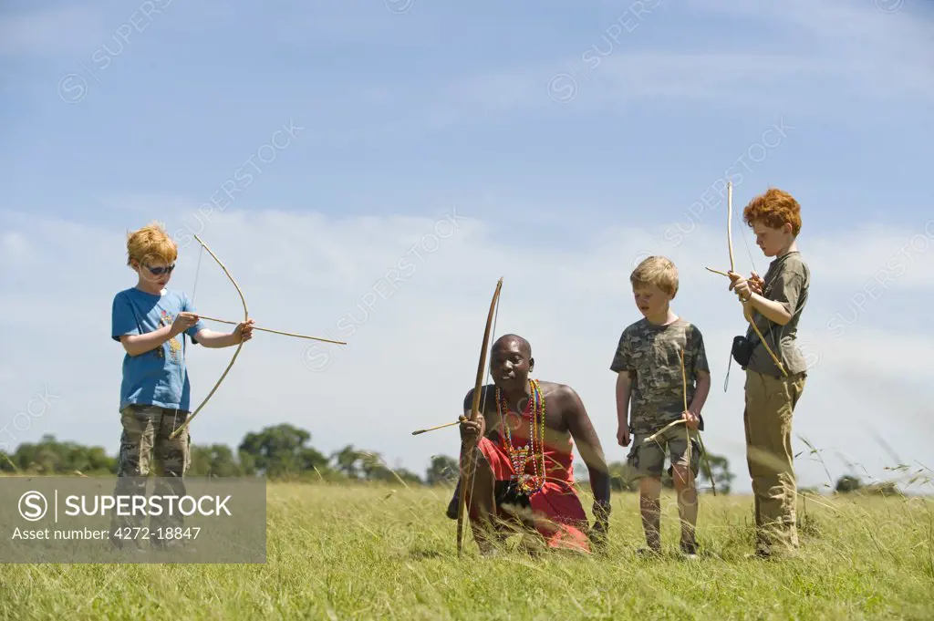 Kenya, Masai Mara.  Safari guide, Salaash Ole Morompi, teaches children archery Maasai style. (MR)