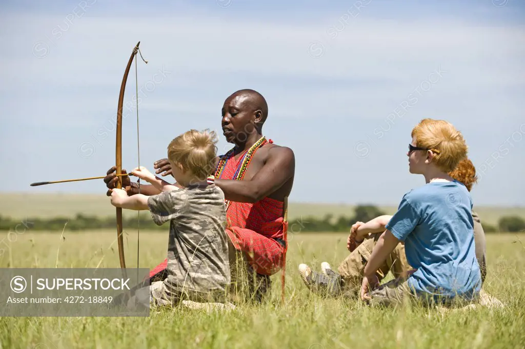 Kenya, Masai Mara.  Safari guide, Salaash Ole Morompi, teaches children archery Maasai style. (MR)