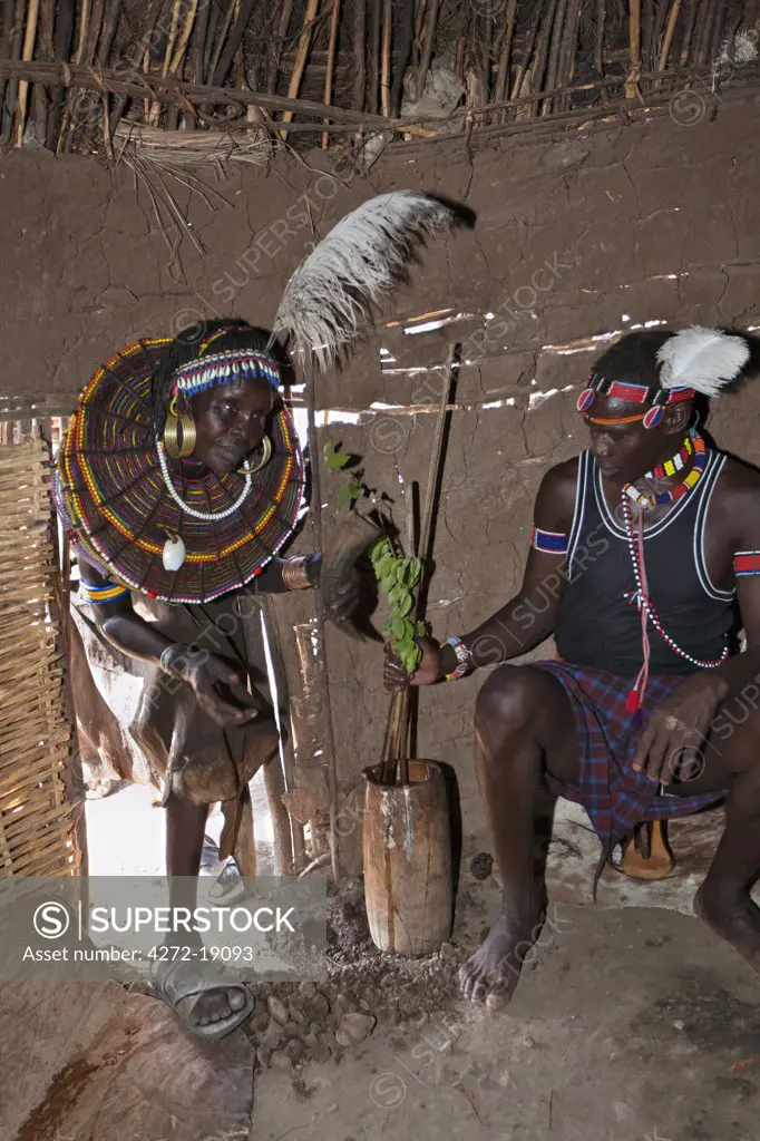 A Pokot woman in the traditional beaded ornaments of her tribe which denote her married status, enters her house. The man is preparing a concoction to bless a pregnant woman for a successful birth.