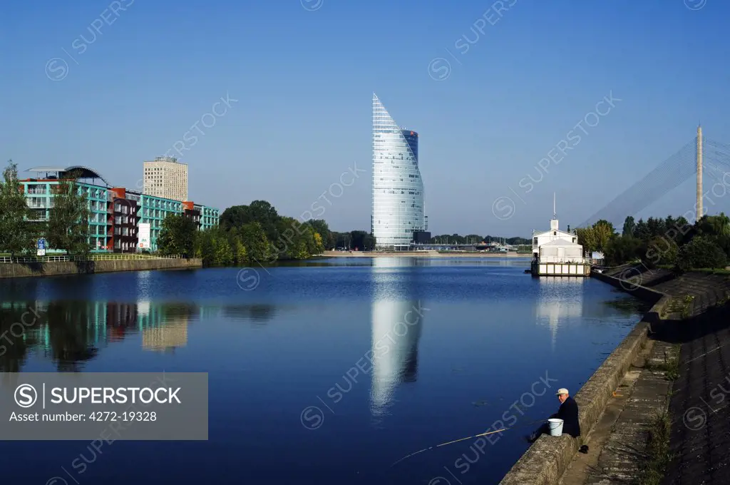 Hansa Bank Headquarters the Saules Akmens building and a man fishing on the banks of the River Daugava