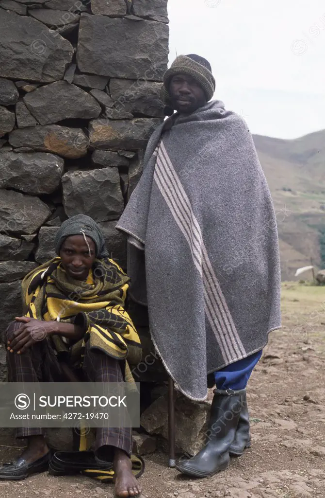 Lesotho men wrap themselves in woollen blankets to keep warm outside a stone shelter.