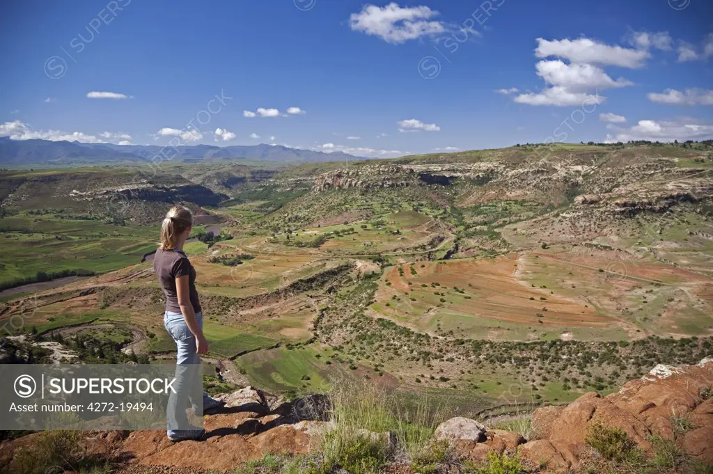 Lesotho, Malealea. A tourist stands at the edge of a cliff and looks over the stunning scenery around the town of Malealea. MR