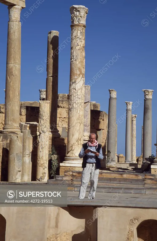 A visitor reads his guidebook on the stage of the  Roman Theatre in the ancient city of Leptis Magna.