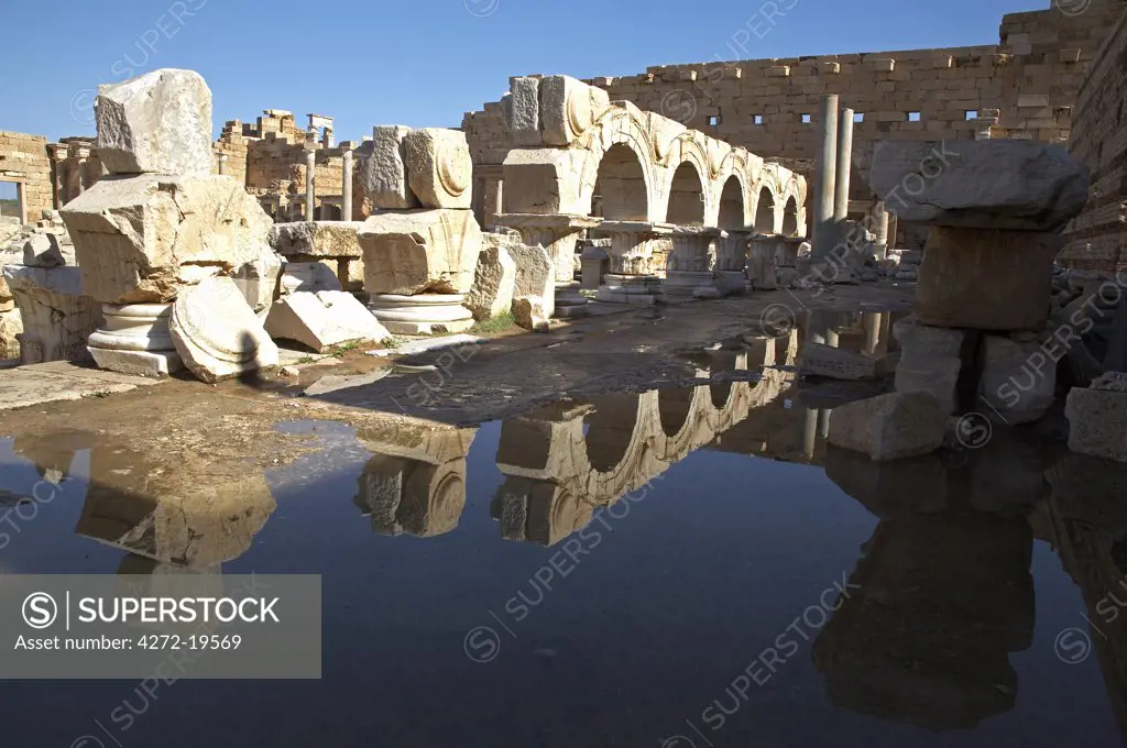The remains of the facades originally built between the arches above the colonnaded porticoes of the Severan Forum, Leptis Magna, reflected in puddles left by recent rain.