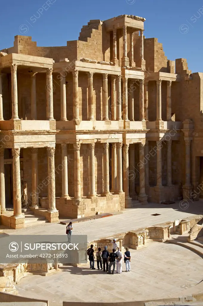 View of the stage and orchestra area of the heavily restored Theatre at Sabratha, Libya. The facade behind the stage is one of the most exceptional in the Roman world. A group in the foreground are admiring the reliefs carved into one of the three concave niches.