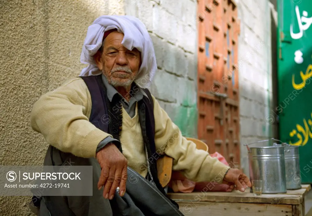 Tripoli, Libya; An elderly Libyan vendor of dried legumesin traditional clothing takes a break beside his shop to drink a cup of dark strong tea and smoke a cigarette in one of the alleys in the town centre