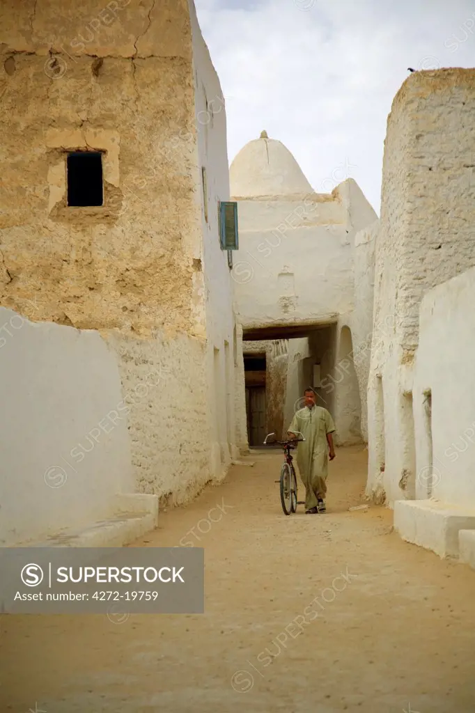 Ghadames, Libya; A man walking with his bicycle through unique the mud constructed buildings of the oasis old town of Ghadames