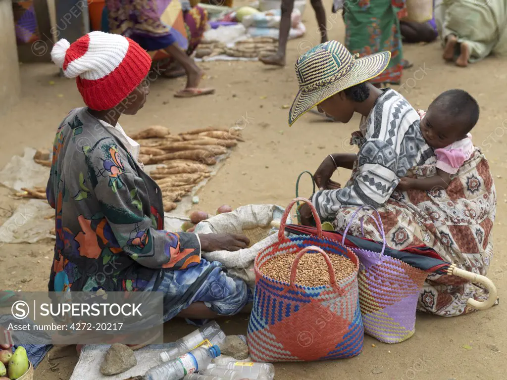 A Malagasy woman with her baby daughter on her back buys food from a street seller at Tsiombe market.