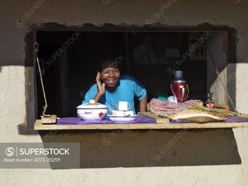 A happy Malagasy woman at the counter of her small rural shop selling tea and a selection of essential inexpensive items.