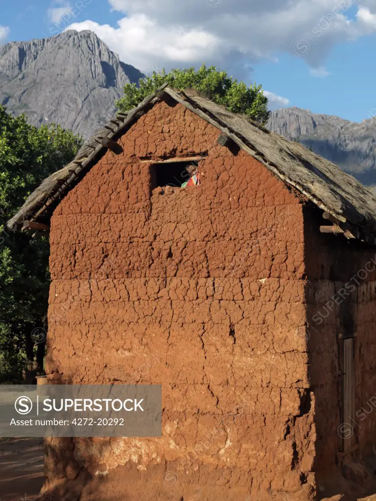 A man peeps out of the top window of a typical double-storied house of the Betsileo people in the Southern Highlands of Madagascar. The bright-red walls are the colour of the earth.