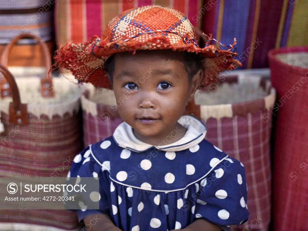 A young girl beside a road-side stall which is offering for sale brightly coloured raffia baskets and hats near Antananarivo, capital of Madagascar.