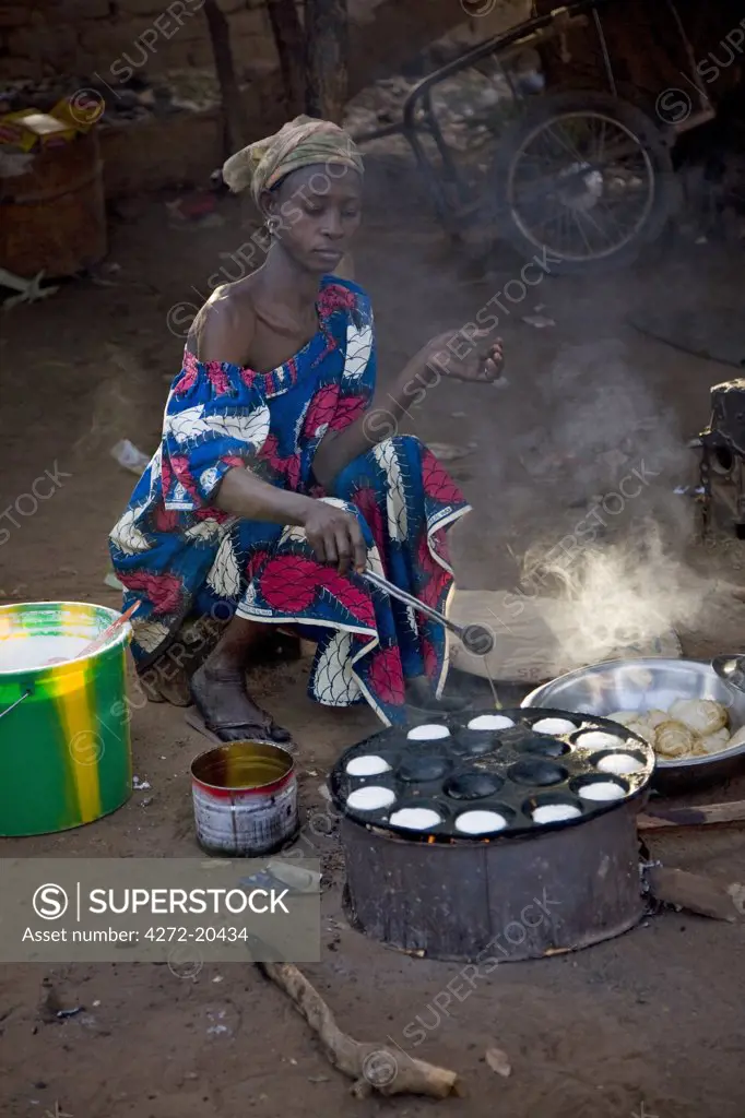 Mali, Bamako, Tinan. A Woman cooks muffins on a wood stove beside the road at the busy weekly market of Tinan situated between Bamako and Segou.